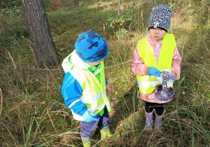 Dzieci spacerują po lesie i szukają śmieci.